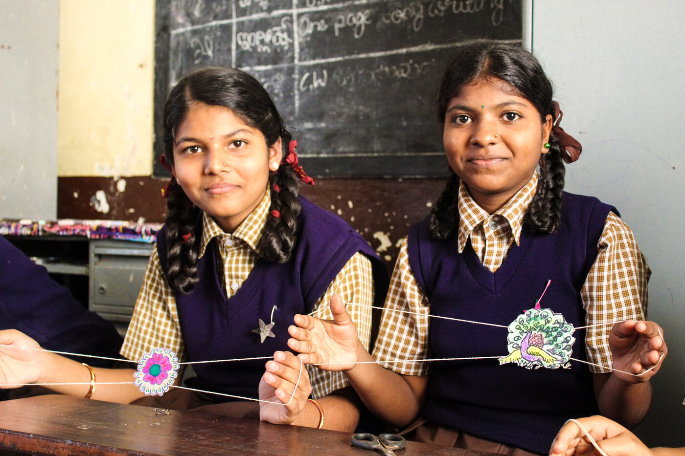 A facilitator working alongside two students at a table with a laptop and hands-on learning materials.
