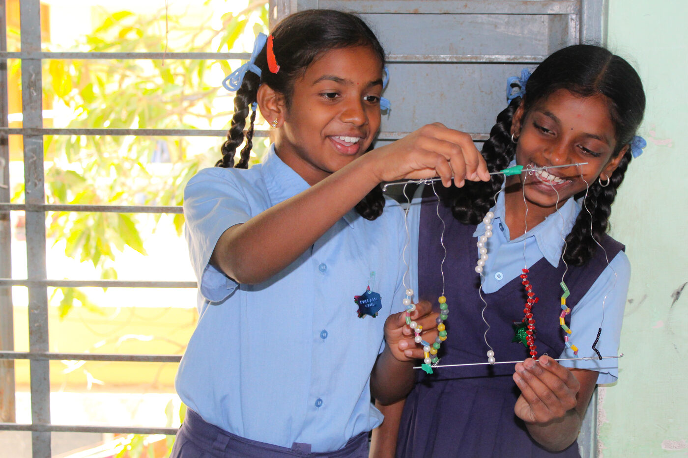 Two girls in school uniform examining and holding up the project they built near a window.