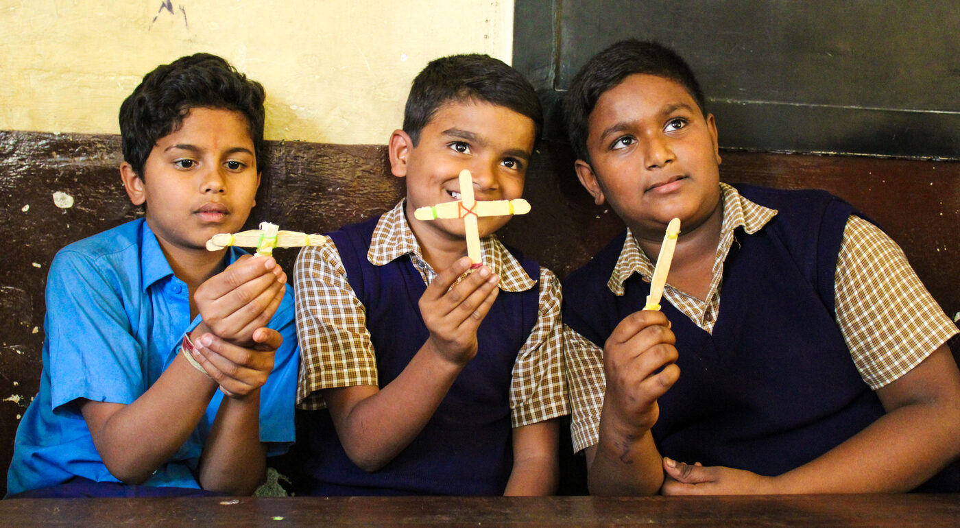 Three students smiling proudly as they hold up the paper models they built in class.